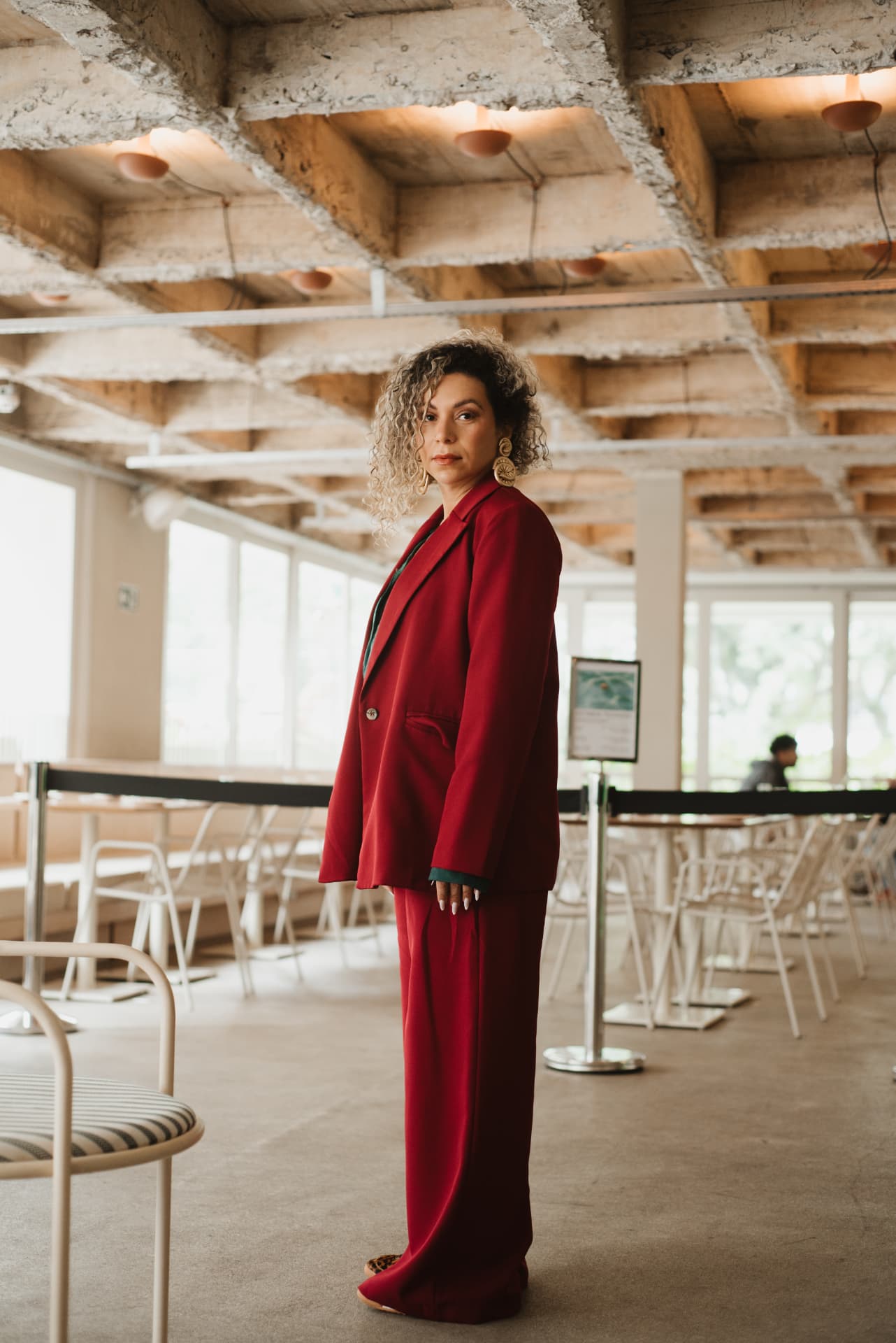 Emy de terno vermelho, em pé, com postura confiante